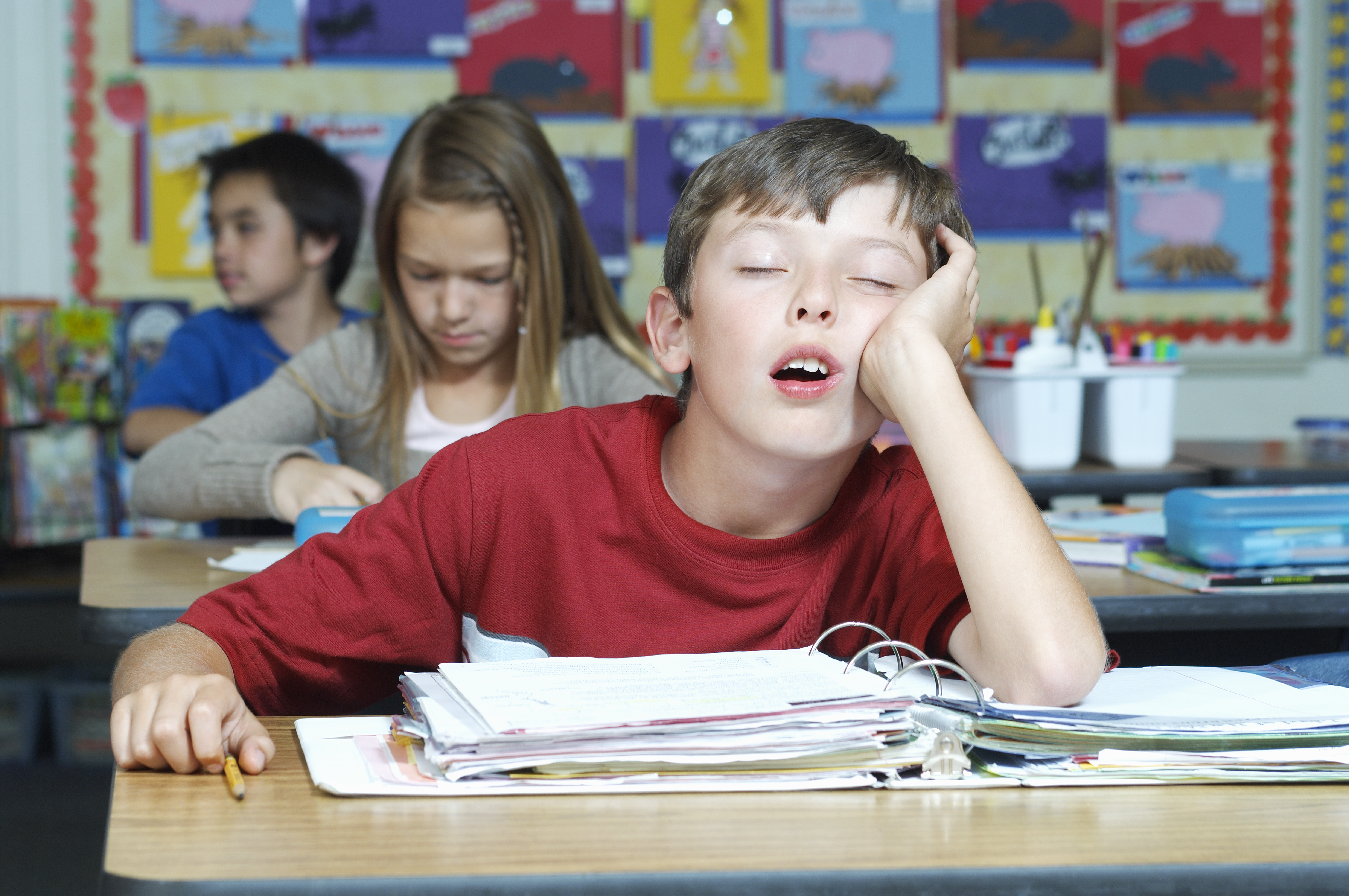 Un enfant dort en classe, le coude appuyé sur son pupitre.