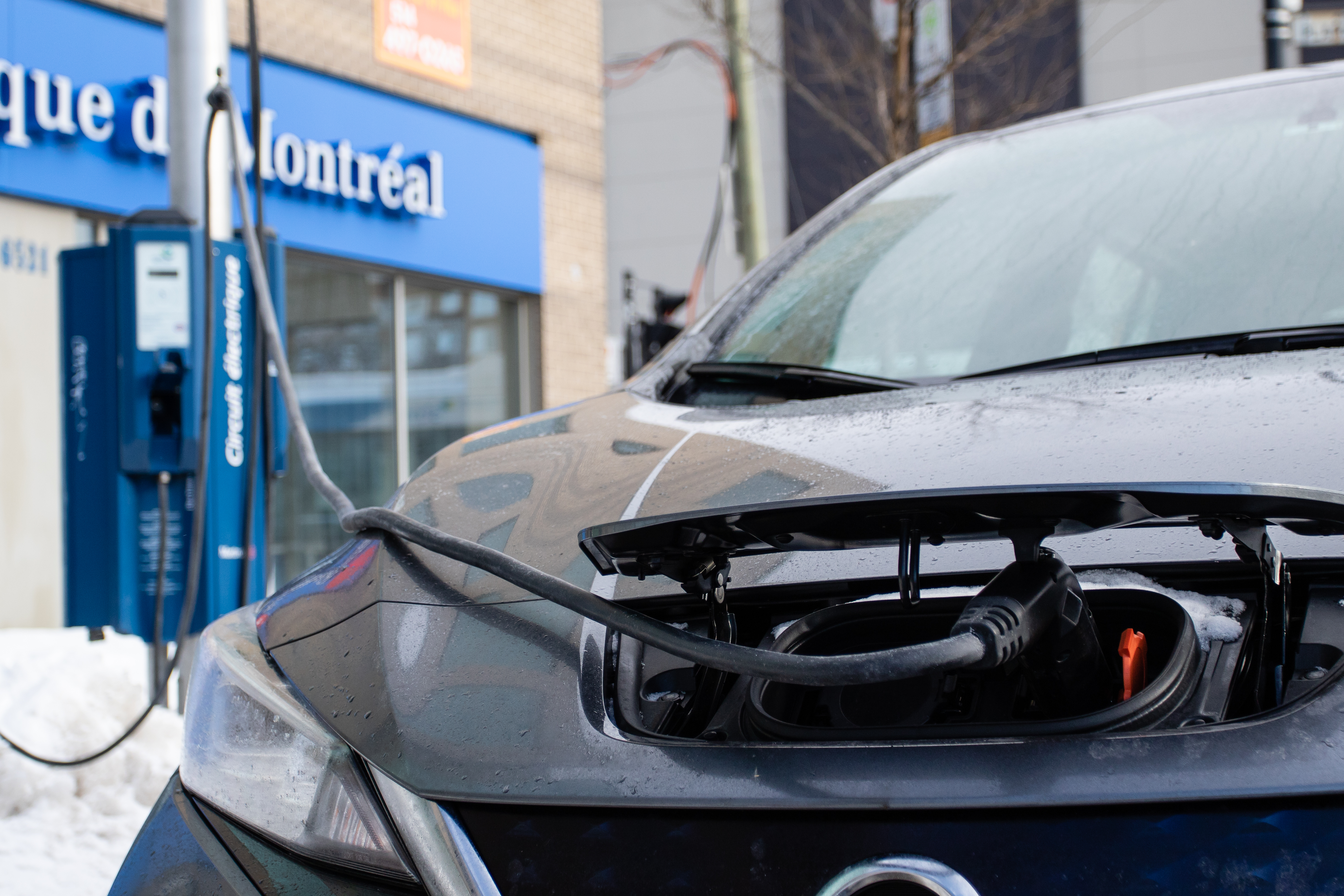 Une voiture branchée sur une borne de recharge de véhicules électriques devant une succursale de la Banque de Montréal.