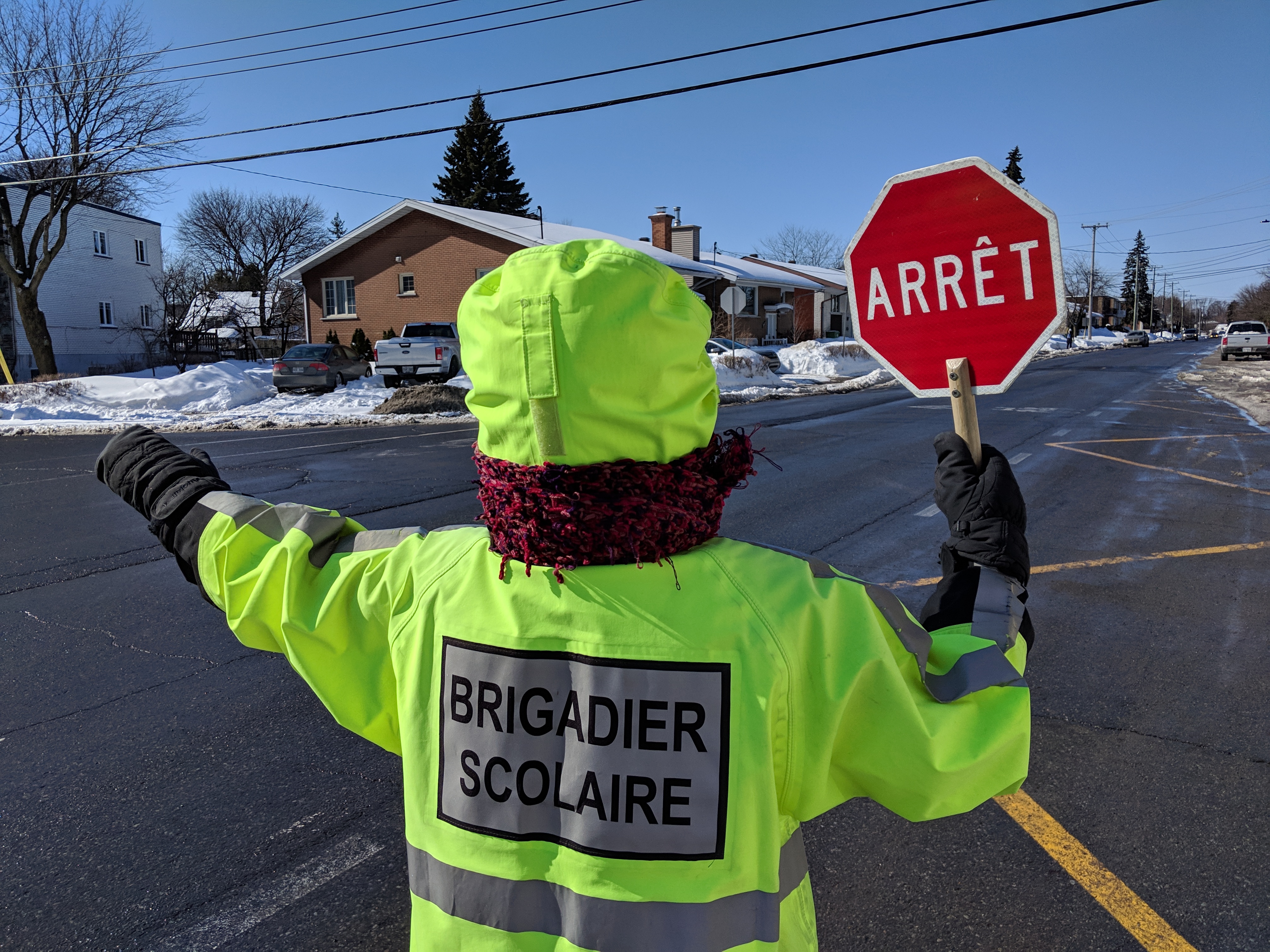 Un brigadier scolaire habillé en vert tenant son panneau d'arrêt levé.