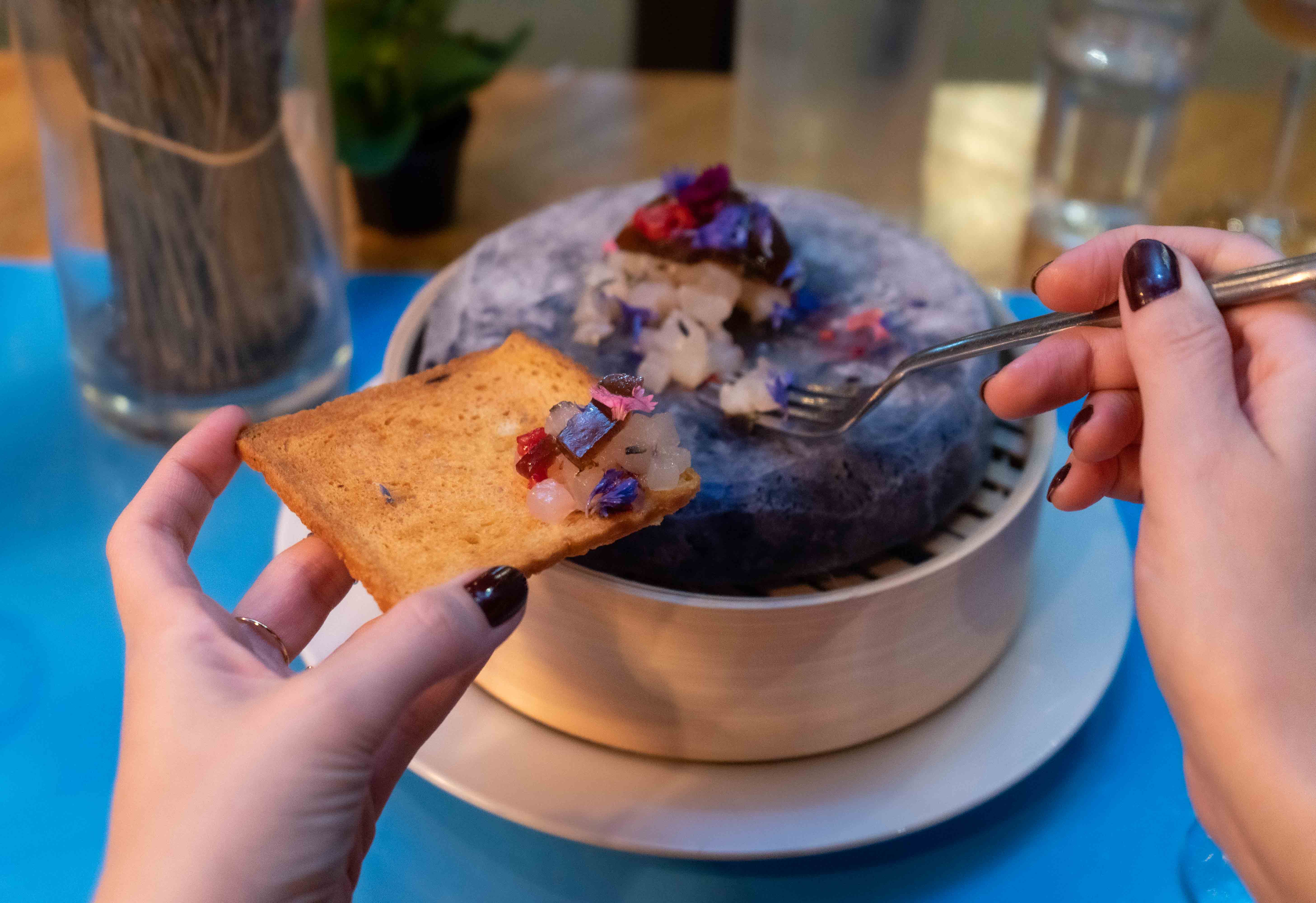 Deux mains tenant fourchette et croûton face à un plat de tartare