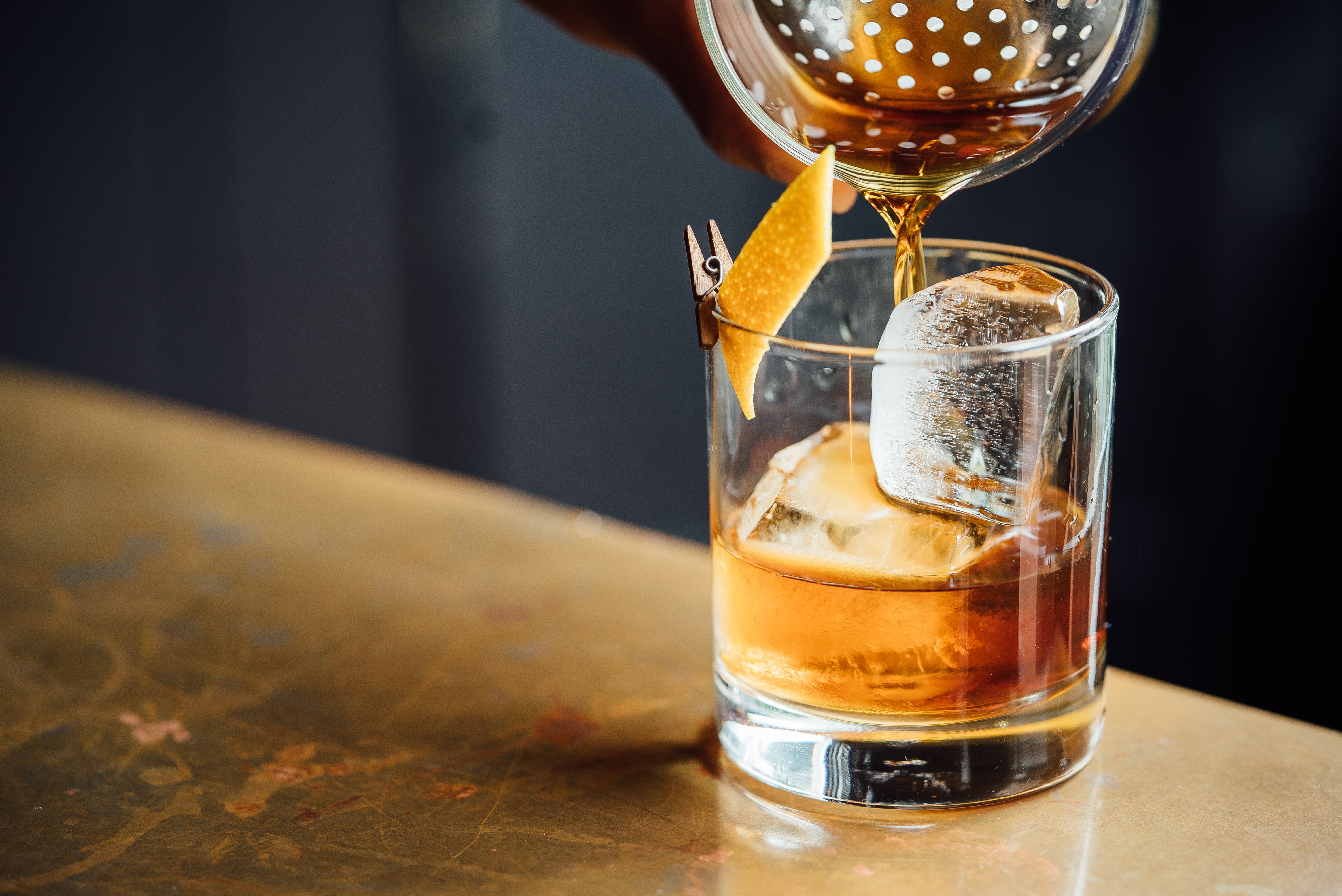 Coquetelier versant un negroni dans un verre garni d'un zeste d'orange et d'un glaçon