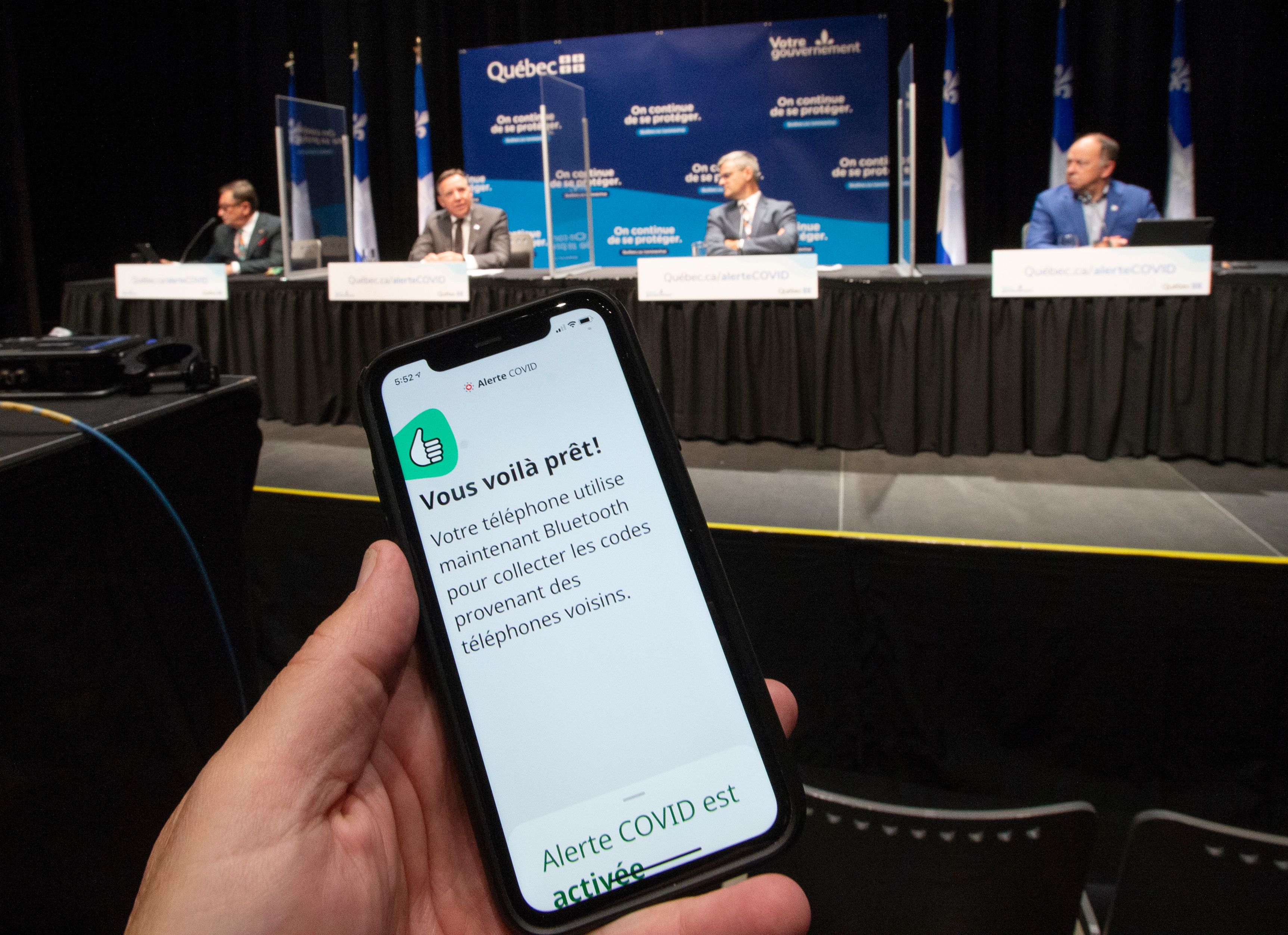 Une main tient un téléphone montrant l'application Alerte COVID pendant le point de presse où François Legault a mis au défi les influenceurs du Québec de télécharger l'application Alerte COVID