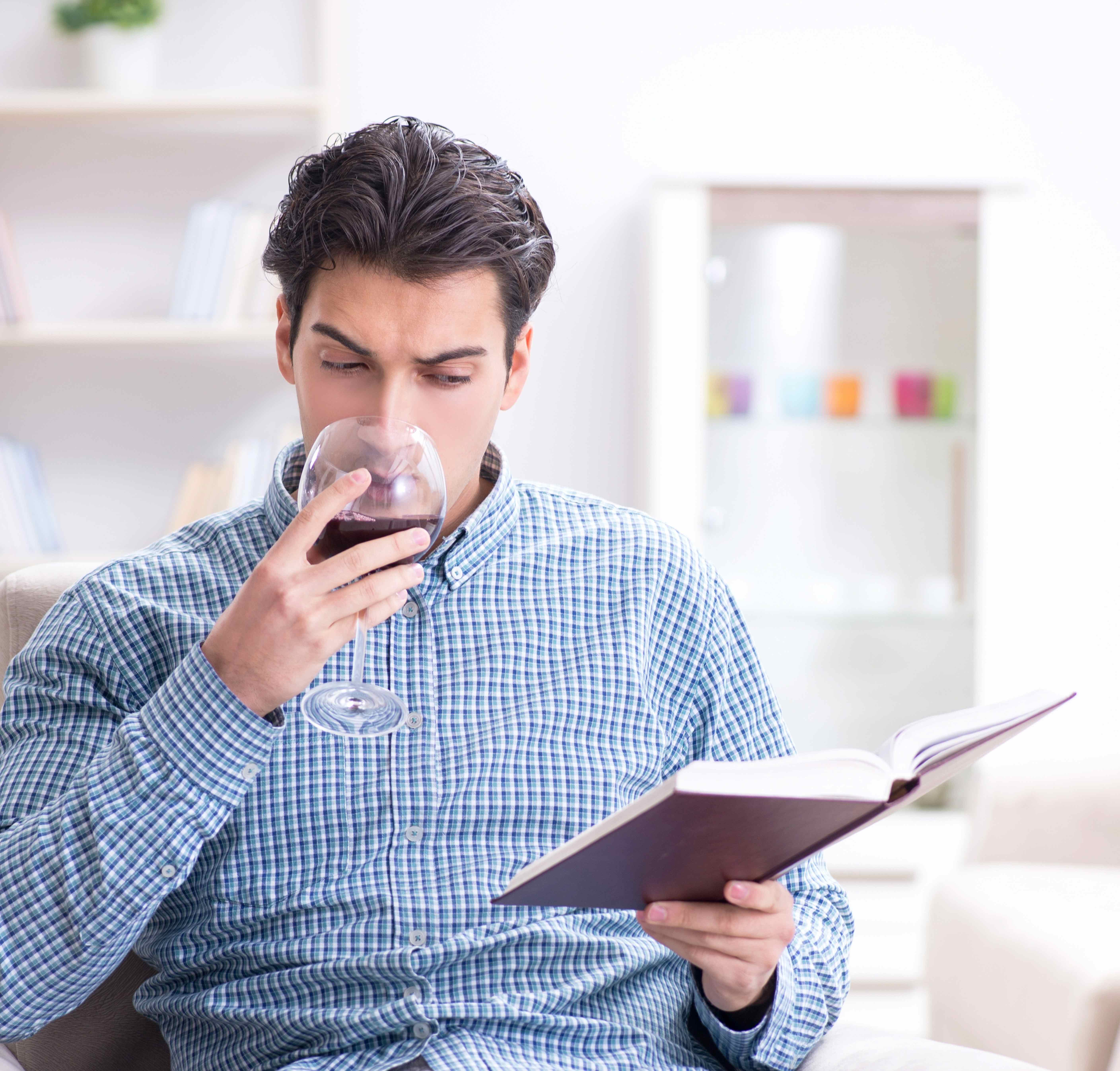 homme qui boit un verre de vin rouge en lisant un livre