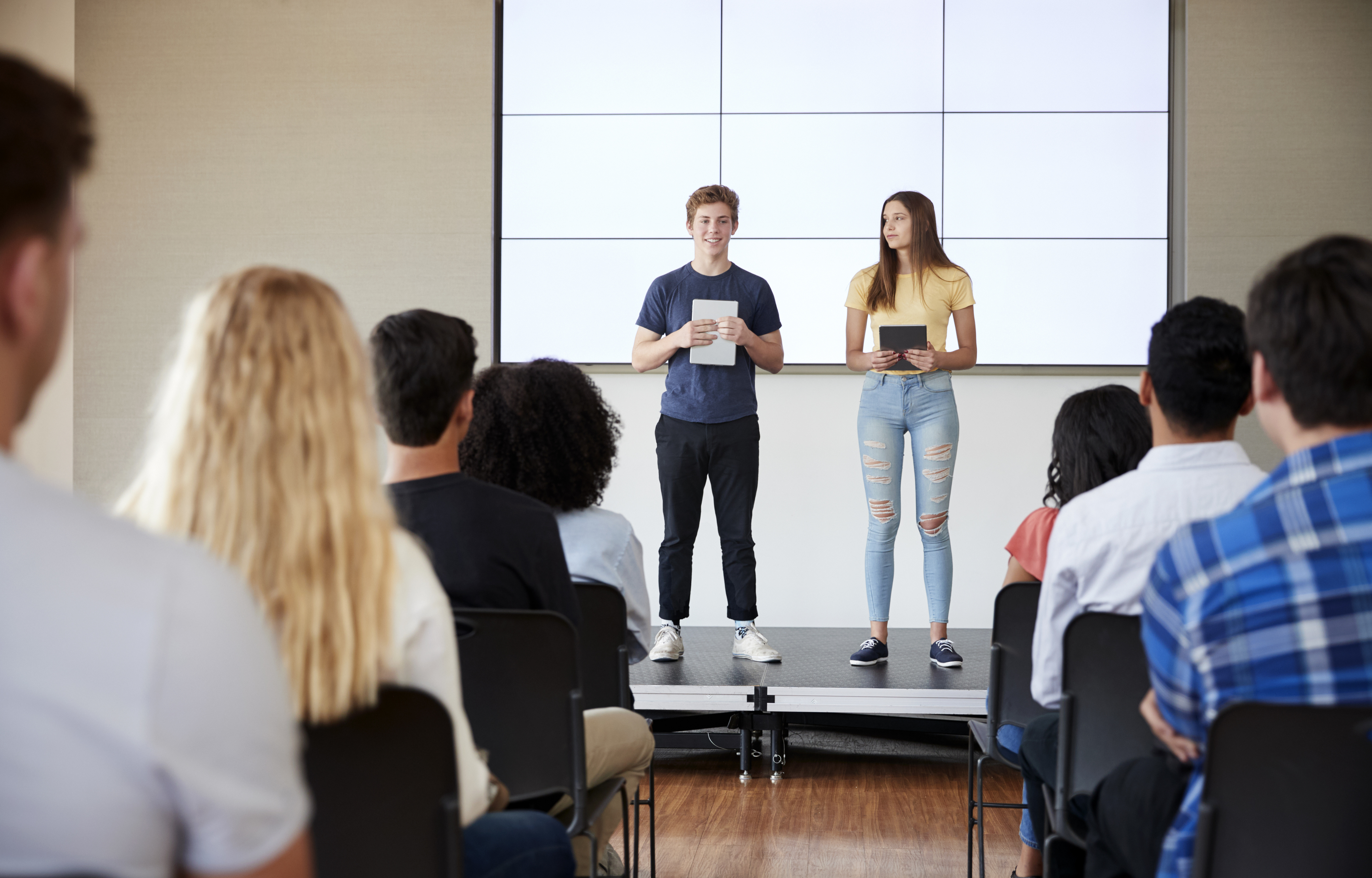 Students With Digital Tablets Giving Presentation To High School Class In Front Of Screen