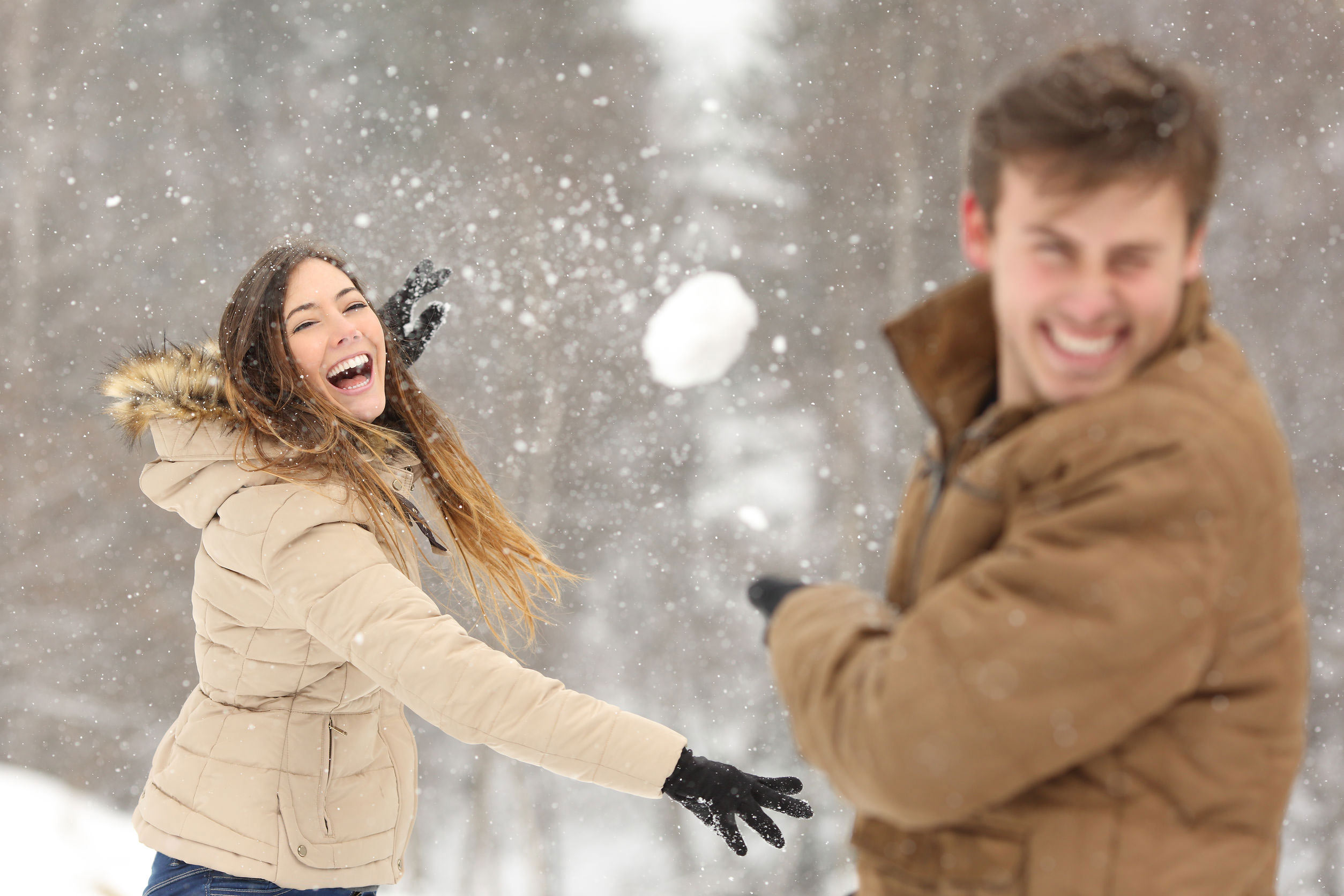Couple jouant avec de la neige et de la petite amie de lancer une balle en vacances d'hiver