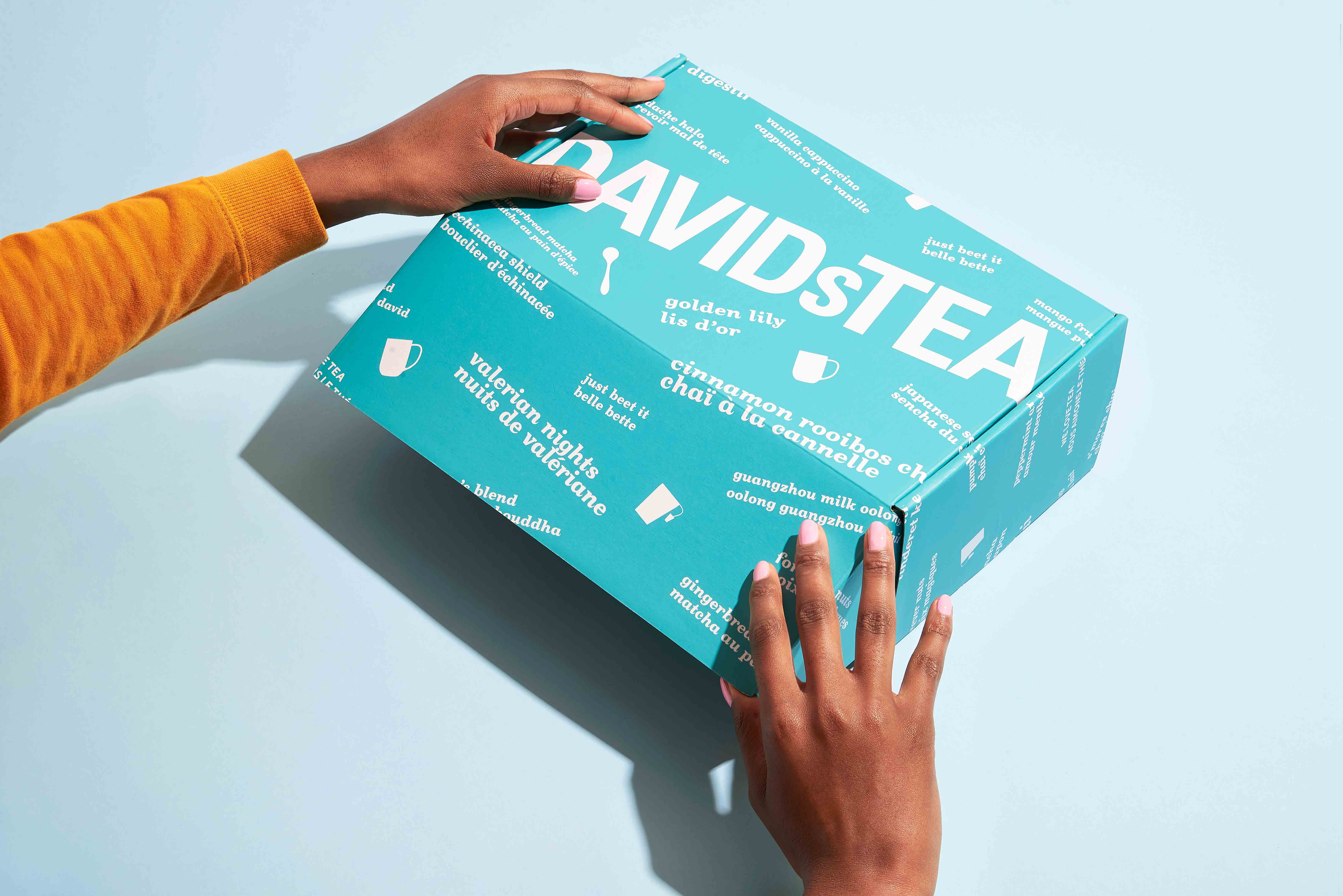 Des mains ouvrant une boîte de thé de couleur verte de la marque DAVIDs TEA