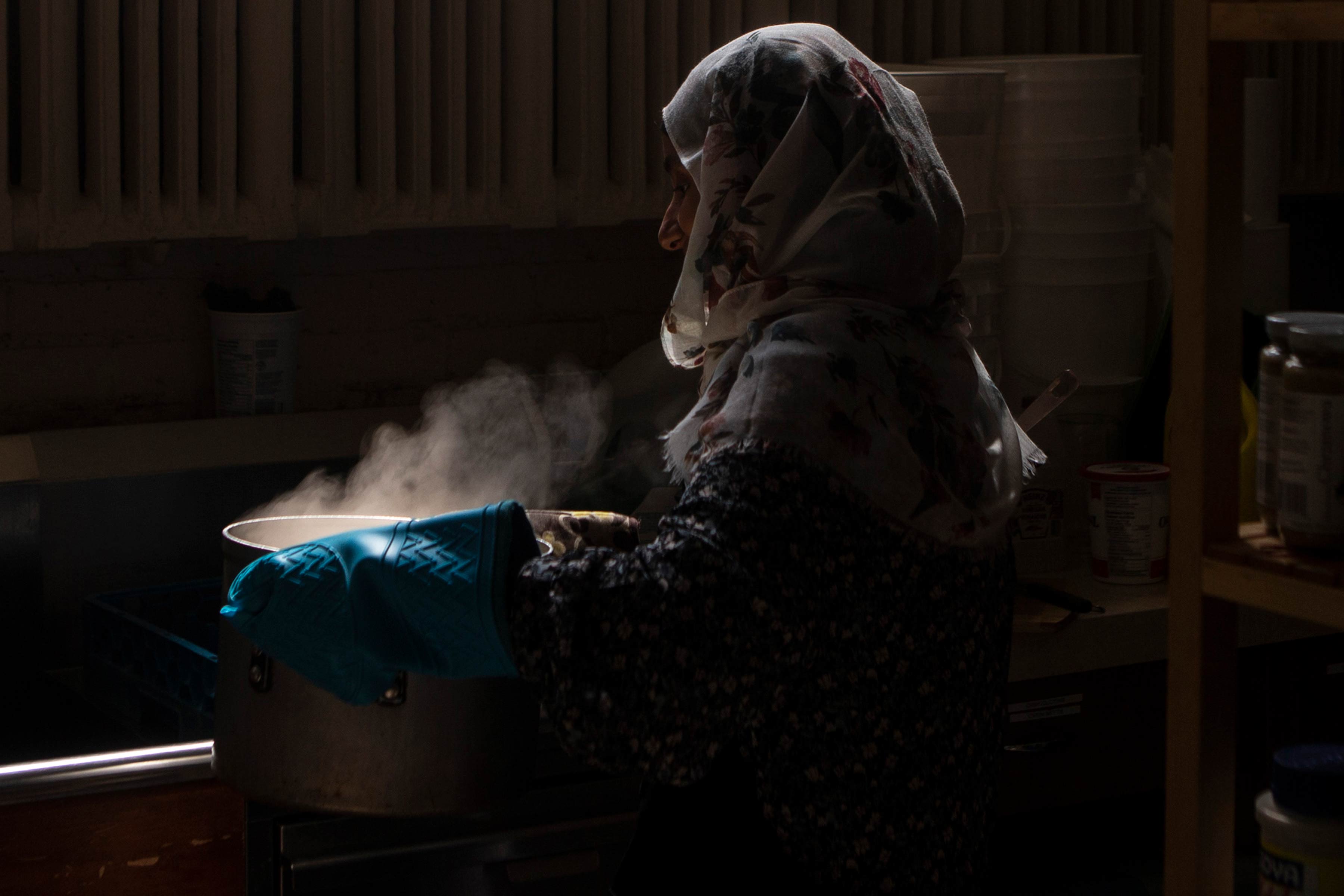 Une femme voilée tenant une casserole fumante à laide de gant en caoutchouc