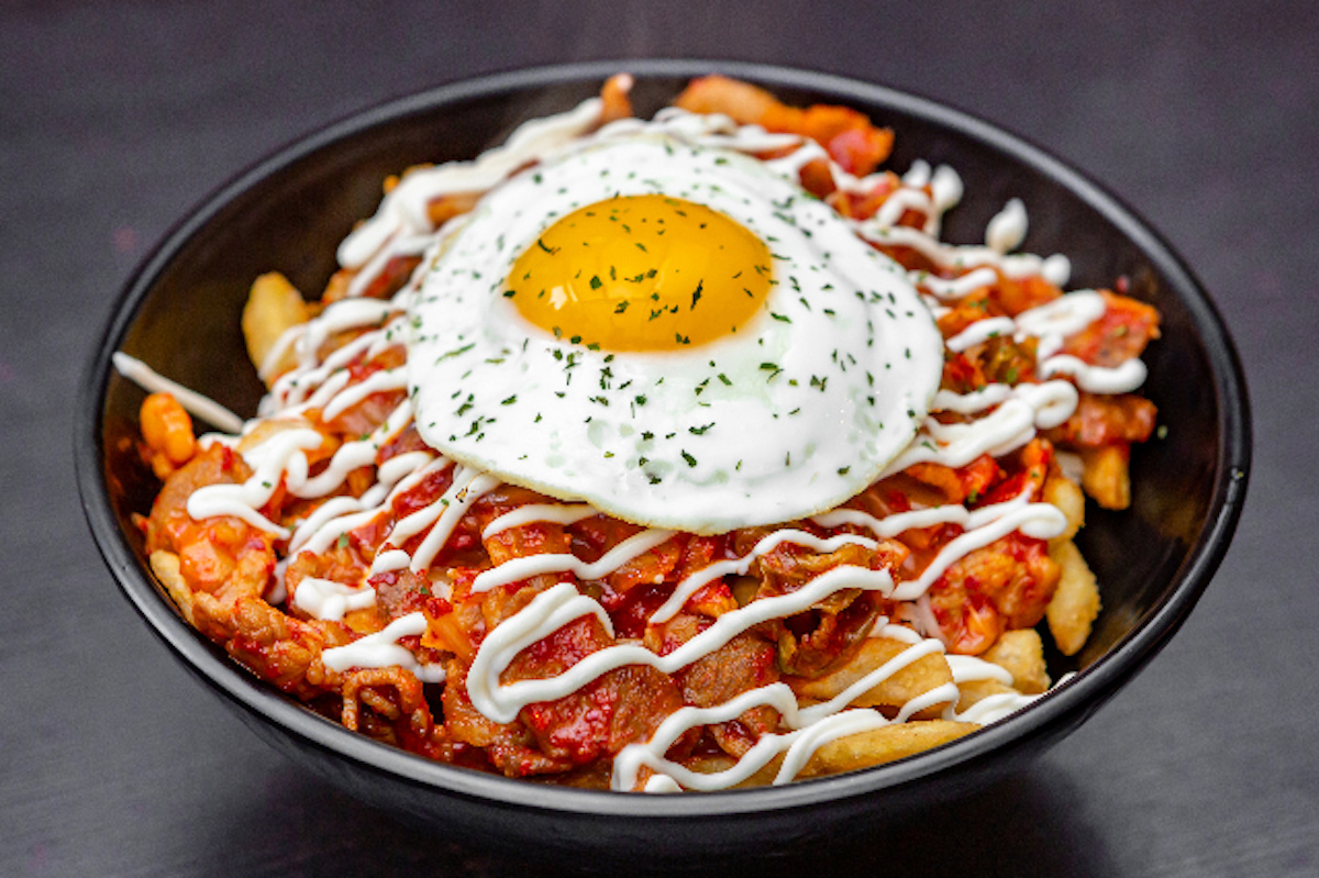 Une poutine dans un bol déposé sur une table de bois. Over head.