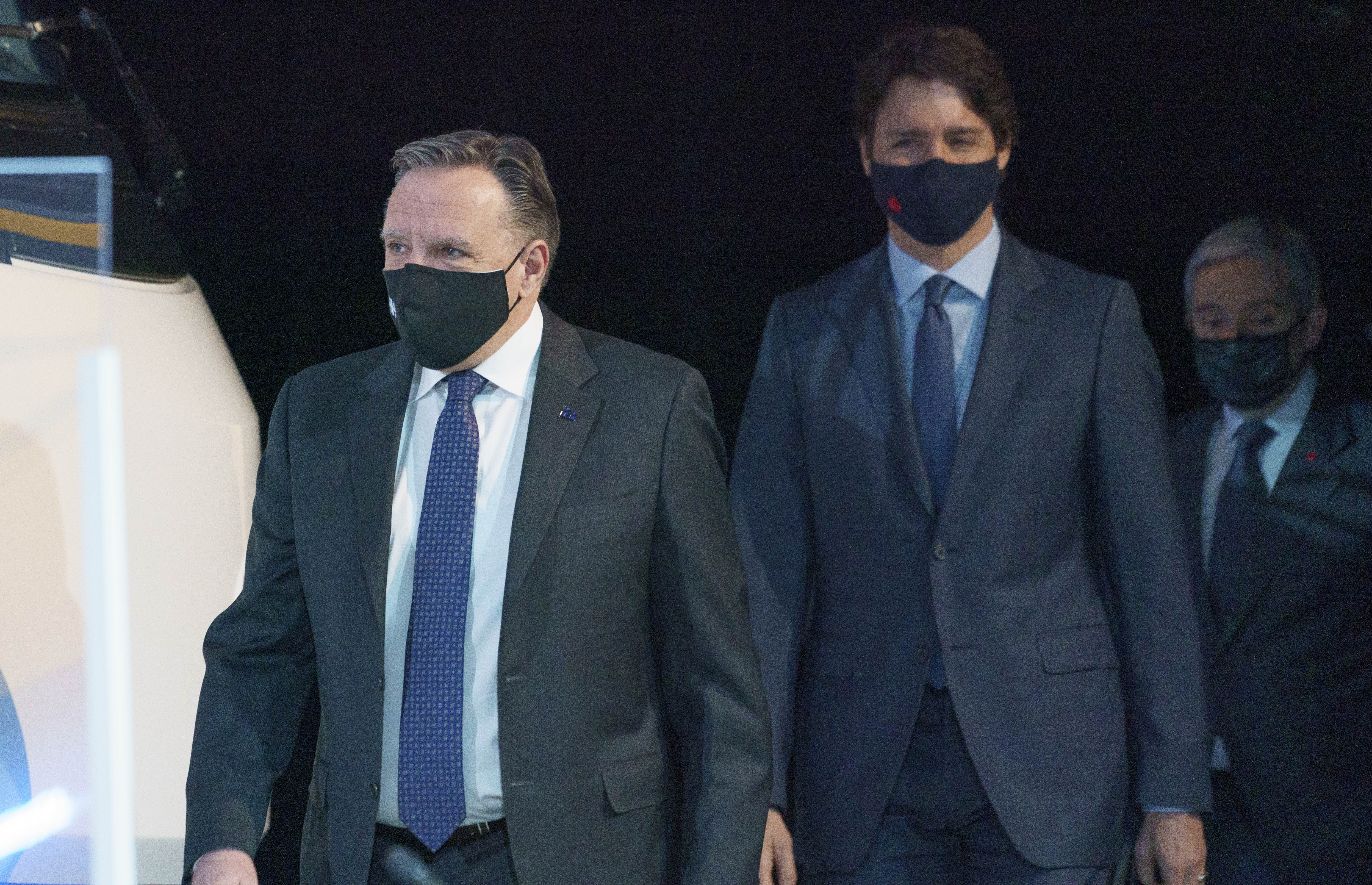 François Legault et Justin Trudeau marchent devant un fond noir, portant des masques
