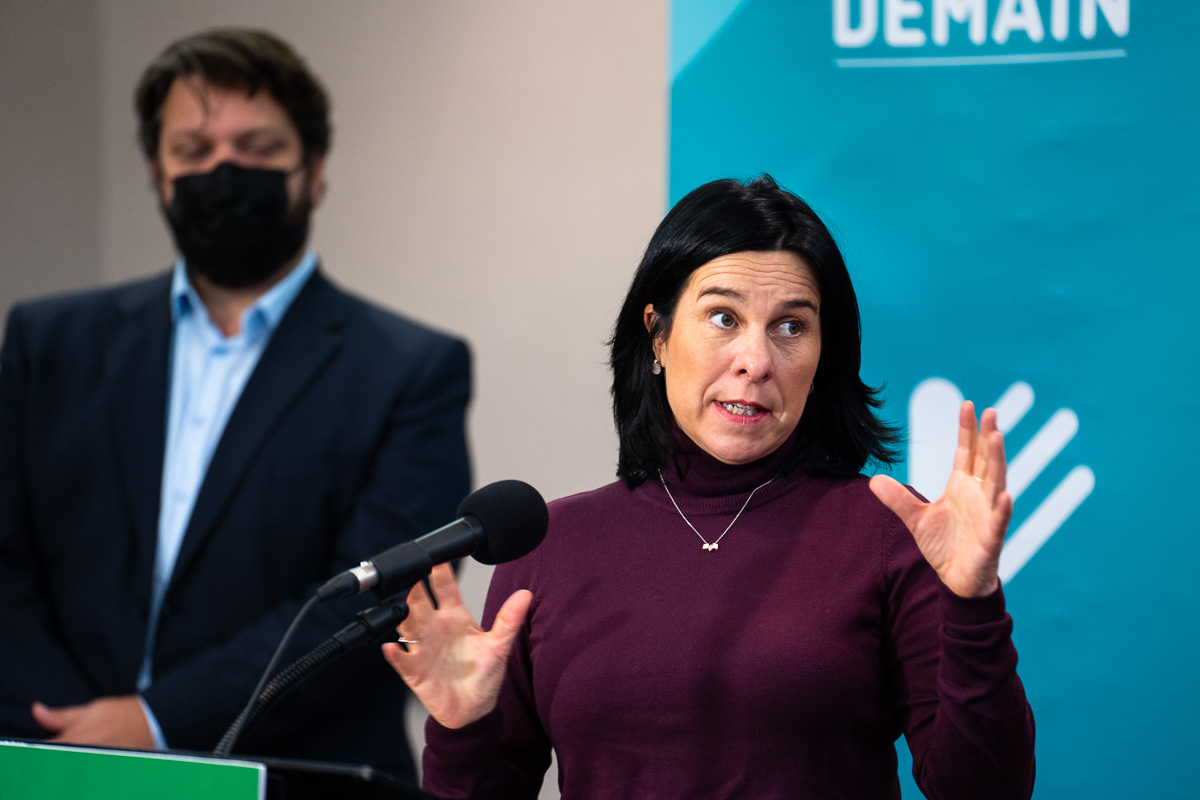 Valérie Plante devant une affiche de Projet Montréal lors d'une annonce concernant le logement à l'ancien hippodrome blue bonnets. En arrière-plan, Éric Alan Caldwell