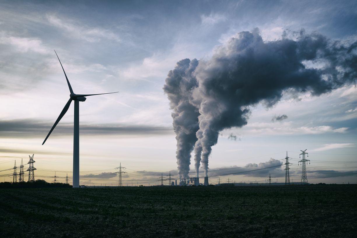 Une usine rejette de la fumée derrière un champ comprenant une éolienne.