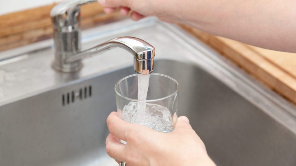 Une personne remplit un verre au robinet de la cuisine.