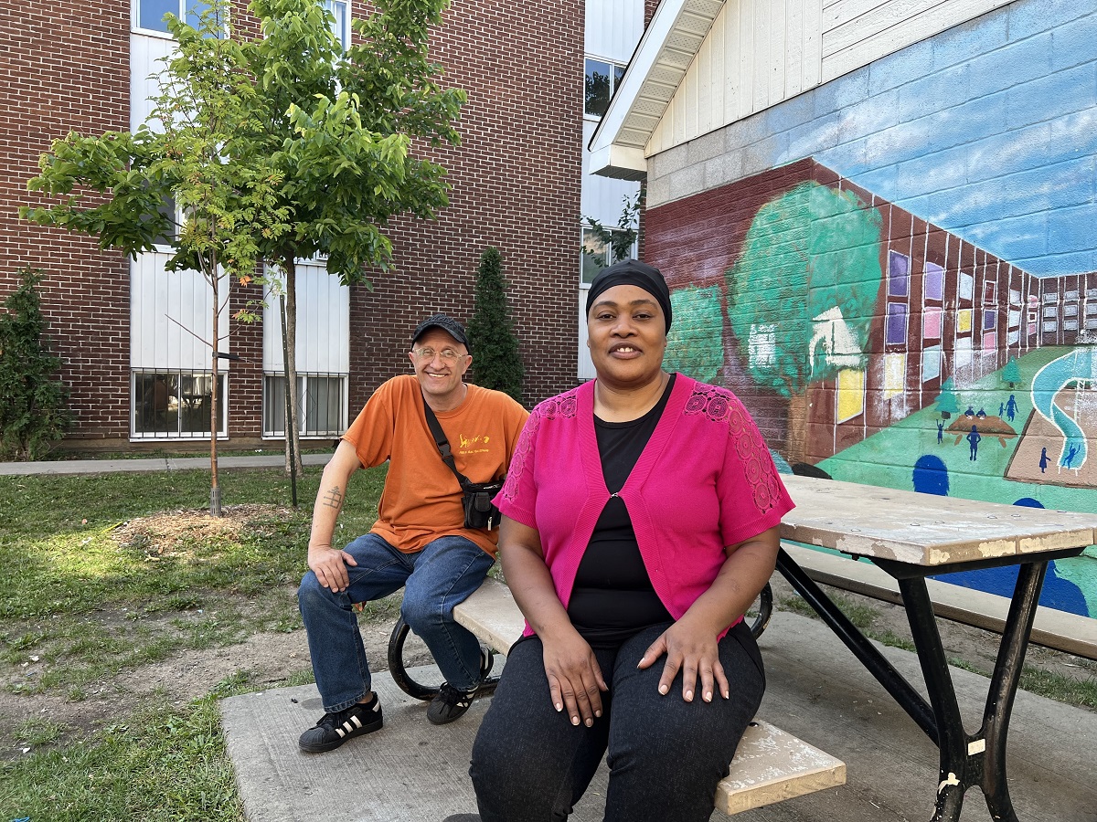 José Trottier et Guerda Calisthene assis sur une table, devant une murale