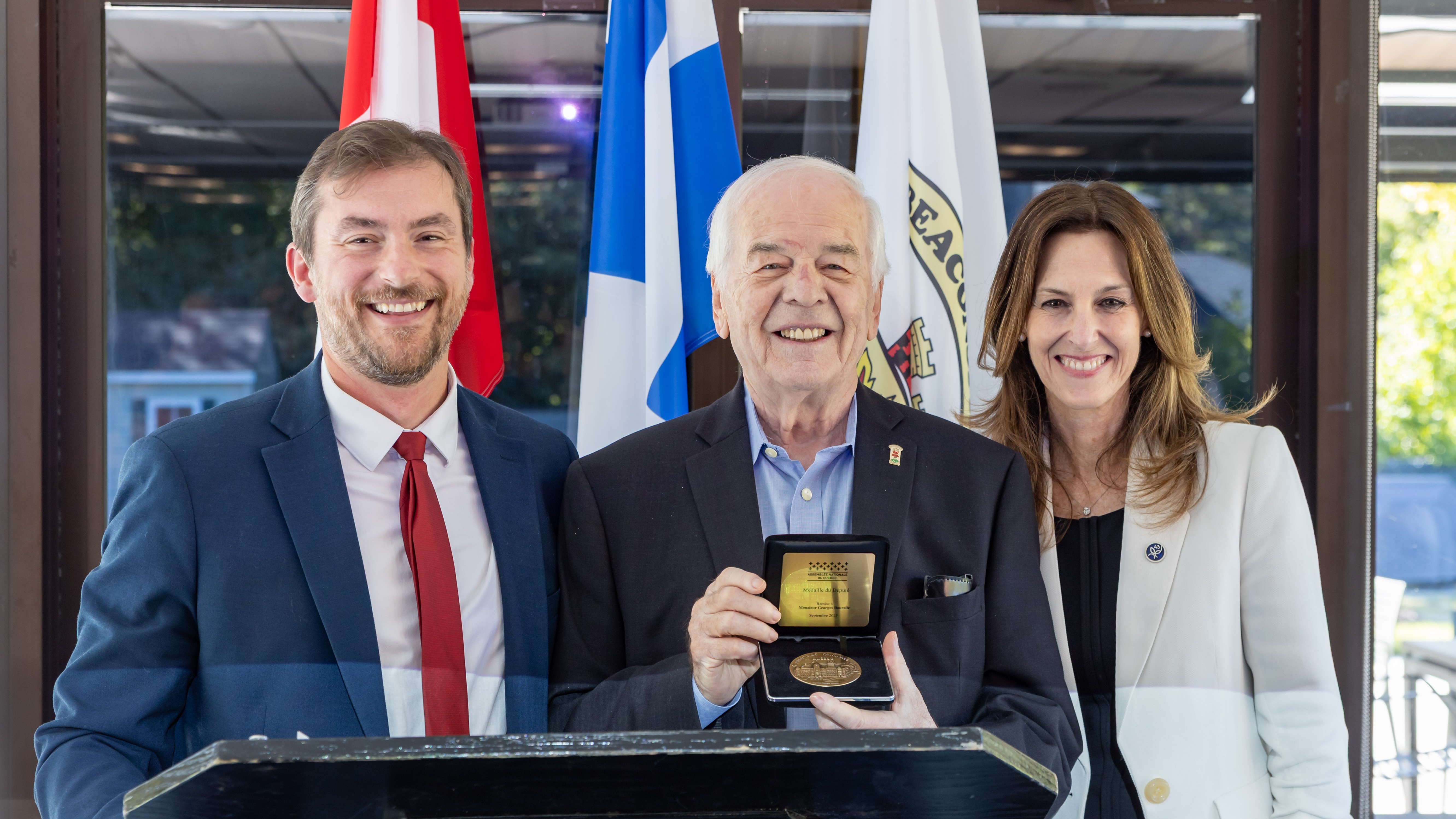 Georges Bourelle montre la médaille d'honneur, accompagné de Gregory Kelley et Brigitte Garceau.
