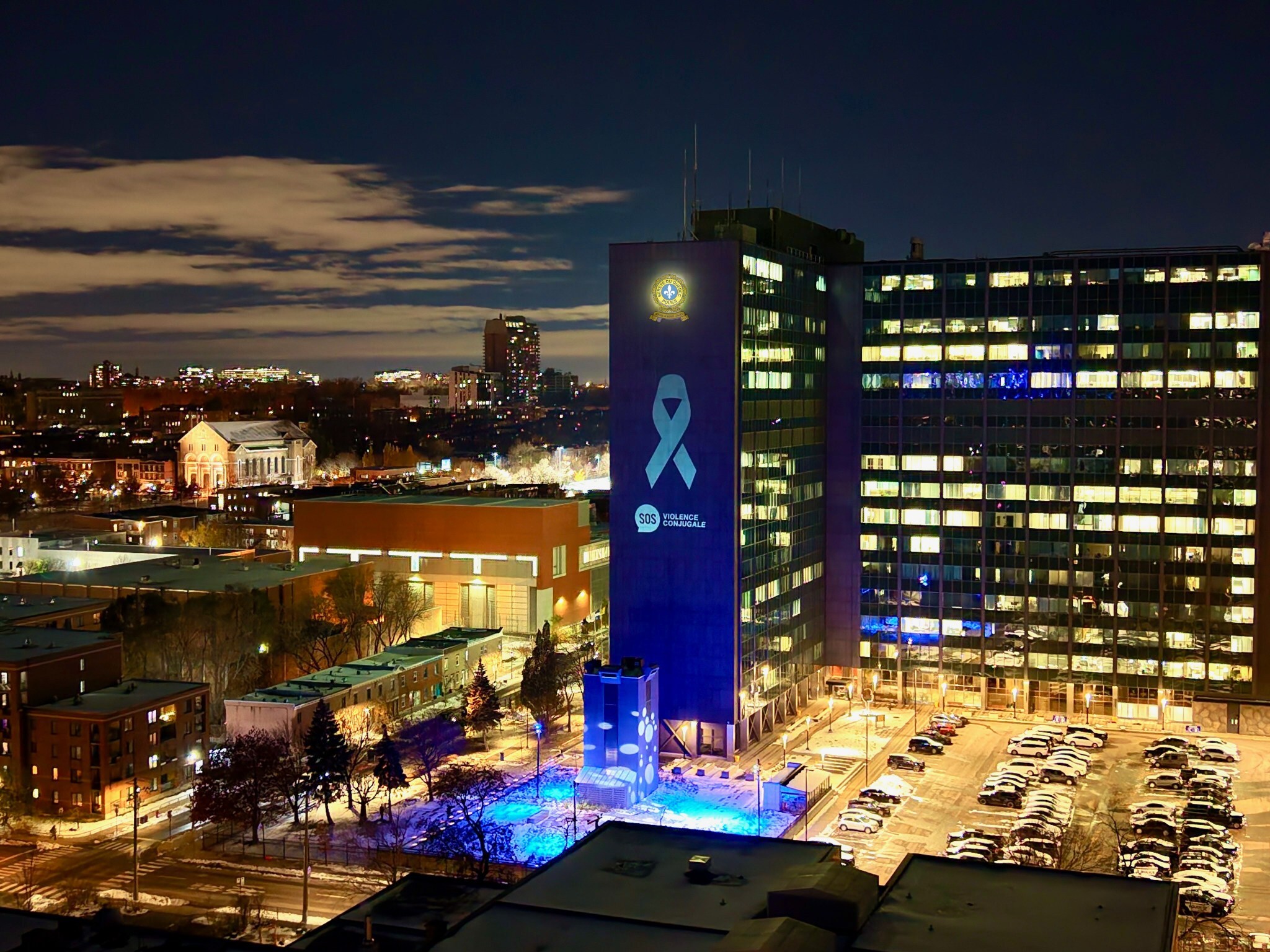 Vue aérienne de la Ville de Montréal montrant l'édifice du quartier général de la SQ. L'édifice est illuminé d'un ruban blanc dans le cadre des 12 jours d'action contre la violence faite aux femmes.