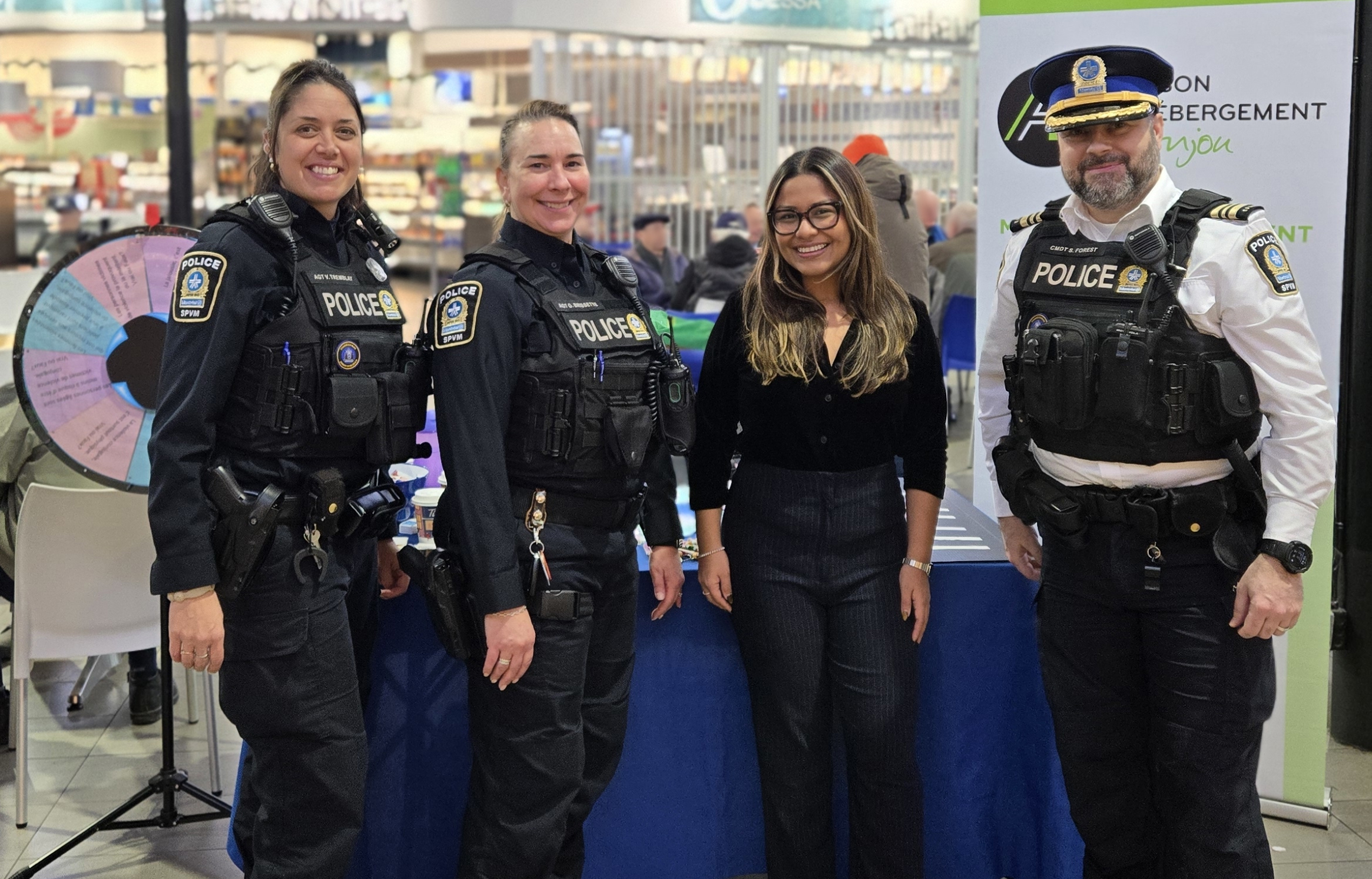 Trois policières et un policier devant un kiosque aux Halles d'Anjou pour une activité de sensibilisation à la violence conjugale.